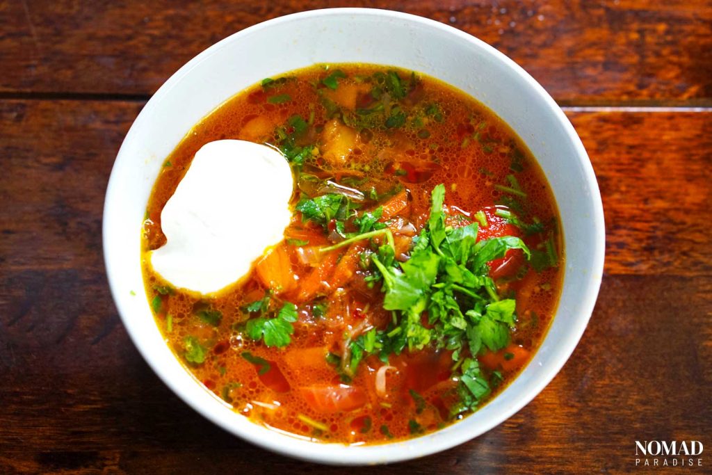 Borsch in a bowl, decorated with fresh parsley and topped with a dollop of sour cream.