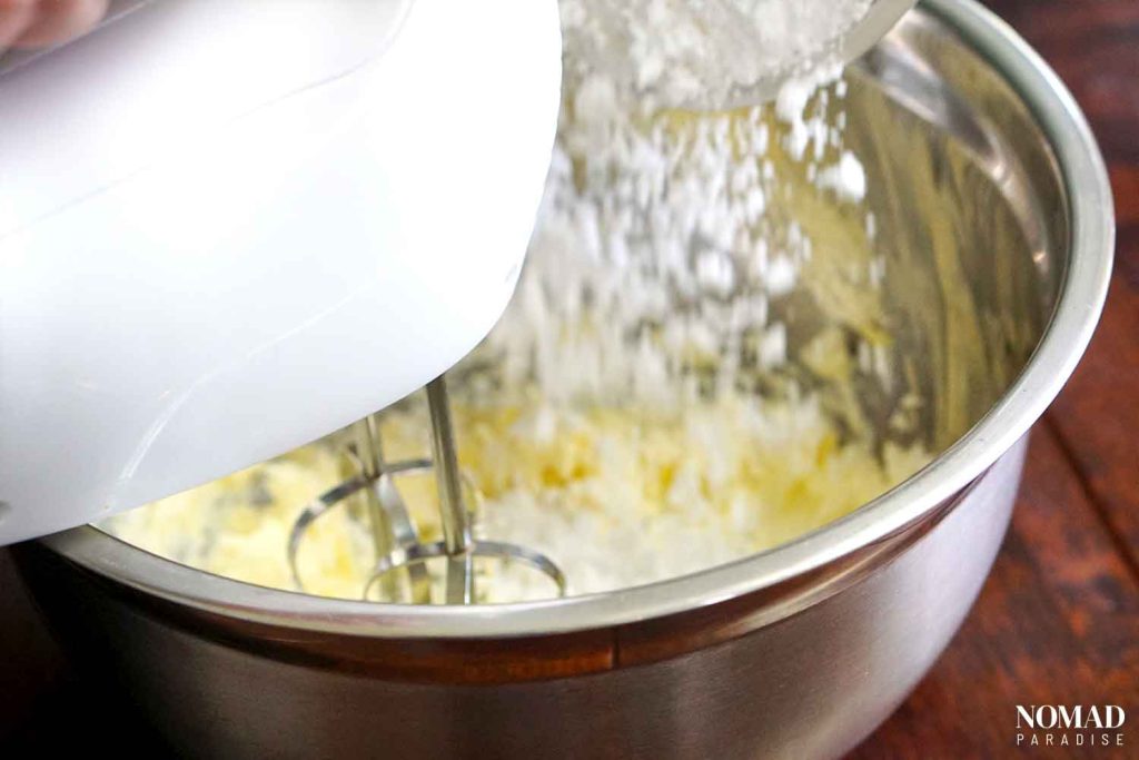 Irish potato candy step by step (mixing softened butter, cream cheese and vanilla in a mixing bowl with a hand mixer while pouring in icing sugar).