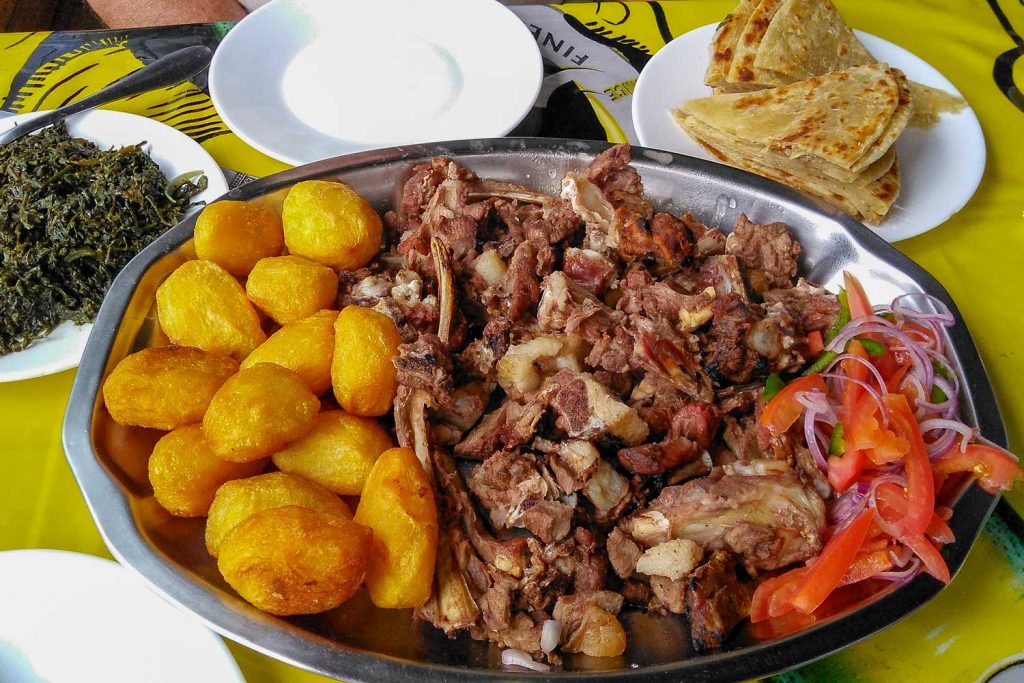 Nyama Choma on a platter served with kachumbari salad, sukuma wiki, chapati and roast potatoes