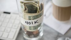 A clear jar labeled 401k holds rolled dollar bills and coins.