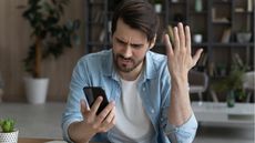 A confused and frustrated man reads something on his smartphone.