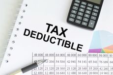 Text Tax Deduction on a notepad among charts and reports on the table.