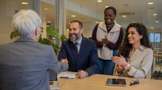 Company executives smile as they sit and stand around a conference room table.