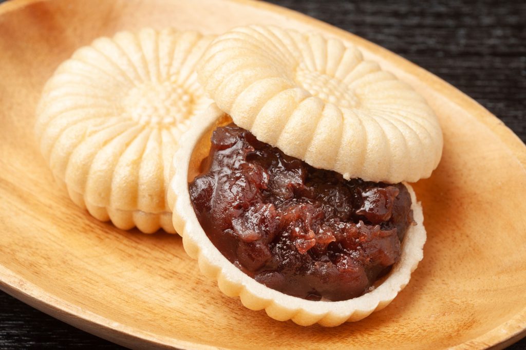 Two Monaka (Sweet Red Bean Paste Sandwiched Between Wafers) in a shallow wooden bowl.