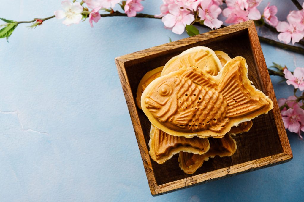 Taiyaki (Fish-Shaped Cake) in a wooden box with some decorative cherry flowers on the table.