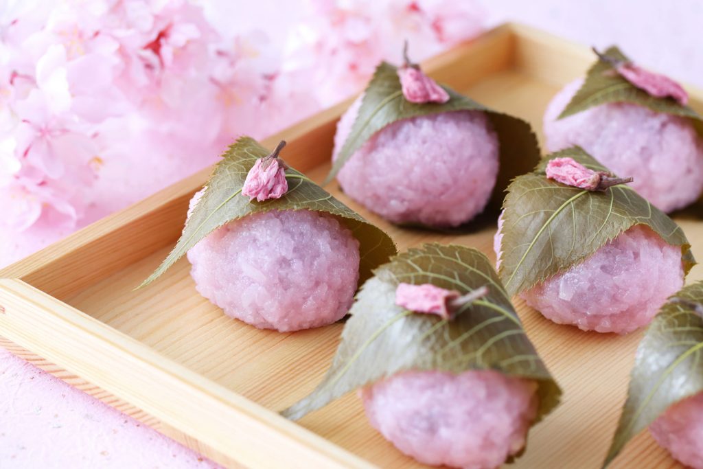 Sakura Mochi (Sweet Pink Mochi with Sweet Red Bean Paste Filling) in a shallow wooden box.
