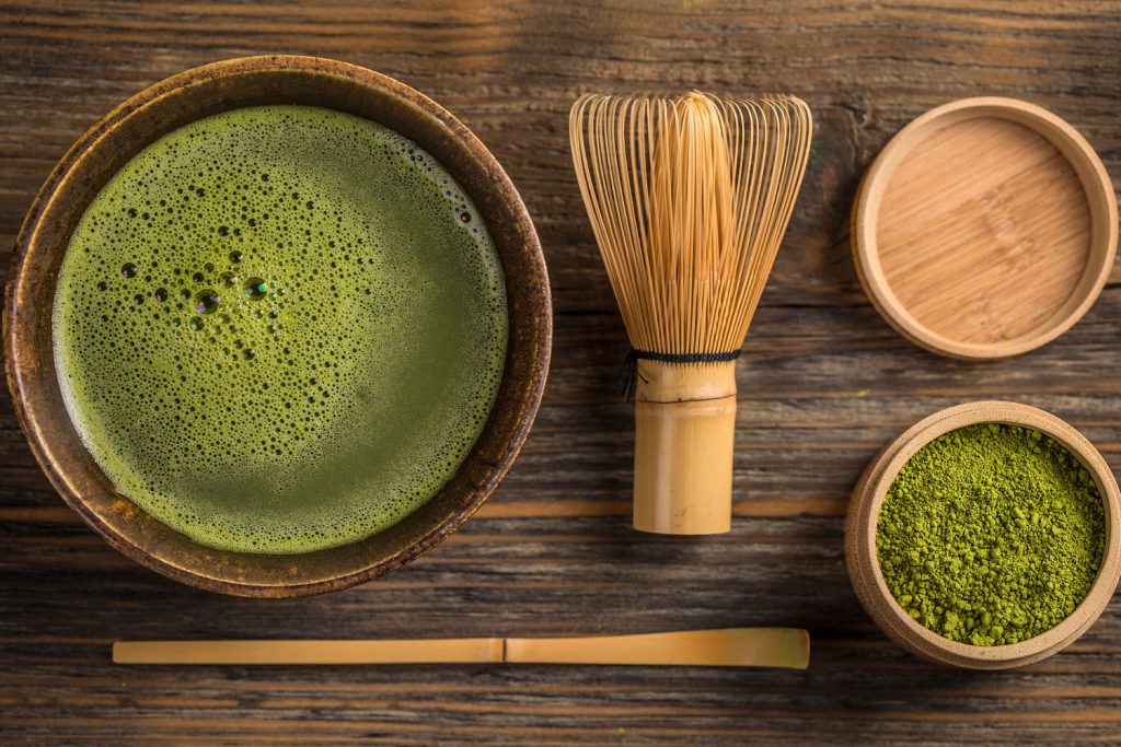 Matcha tea in a bowl, matcha whisk, and match powder in a small bowl.