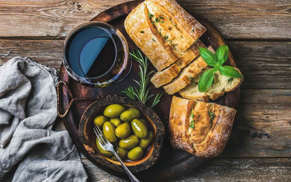 Bread, olives, wine on a wood background depicting the main elements of Mediterranean cuisine: olives, wheat, and grapes