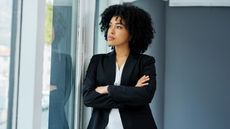 A businesswoman looks thoughtful as she looks out the window of a skyscraper.