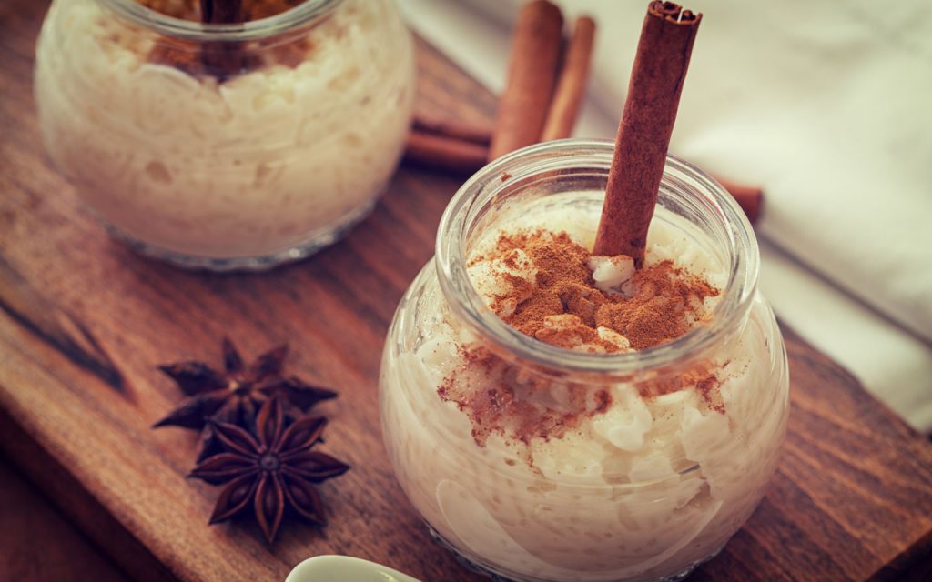 Arroz con leche – rice pudding - in a small glass jar on a wooden board with a cinnamon stick for decoration.
