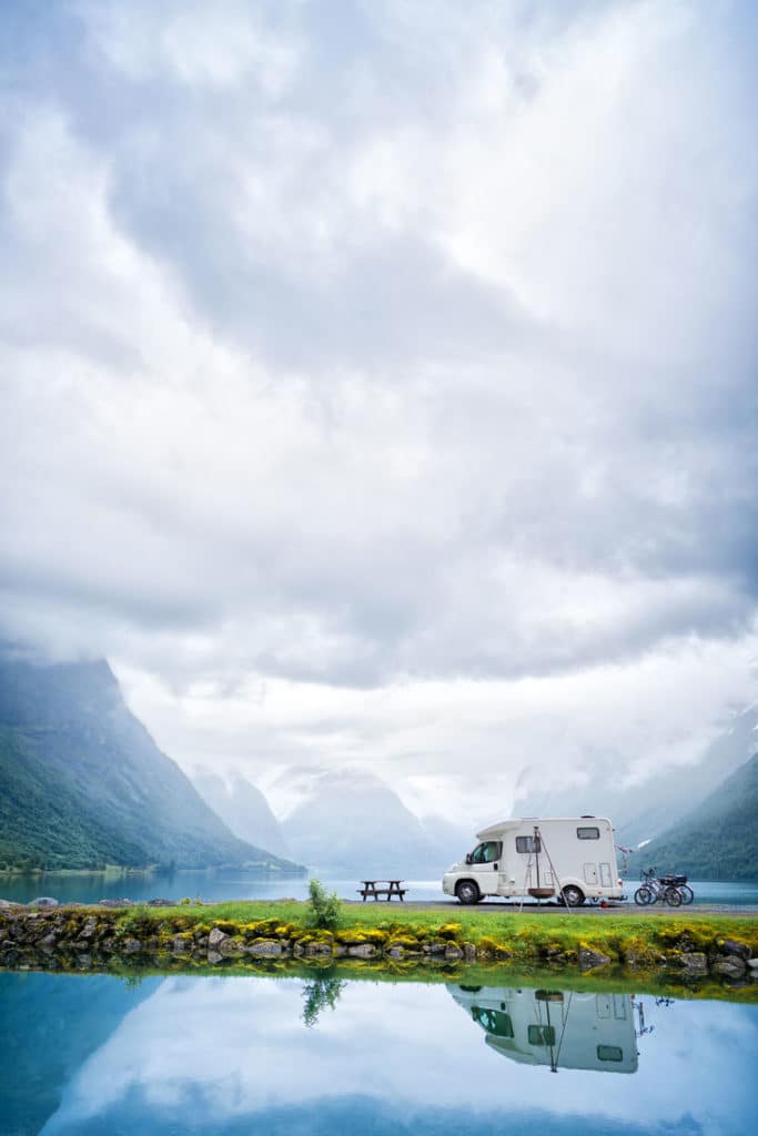 Staycation idea: an RV by a lake and mountains with beautiful scenery.