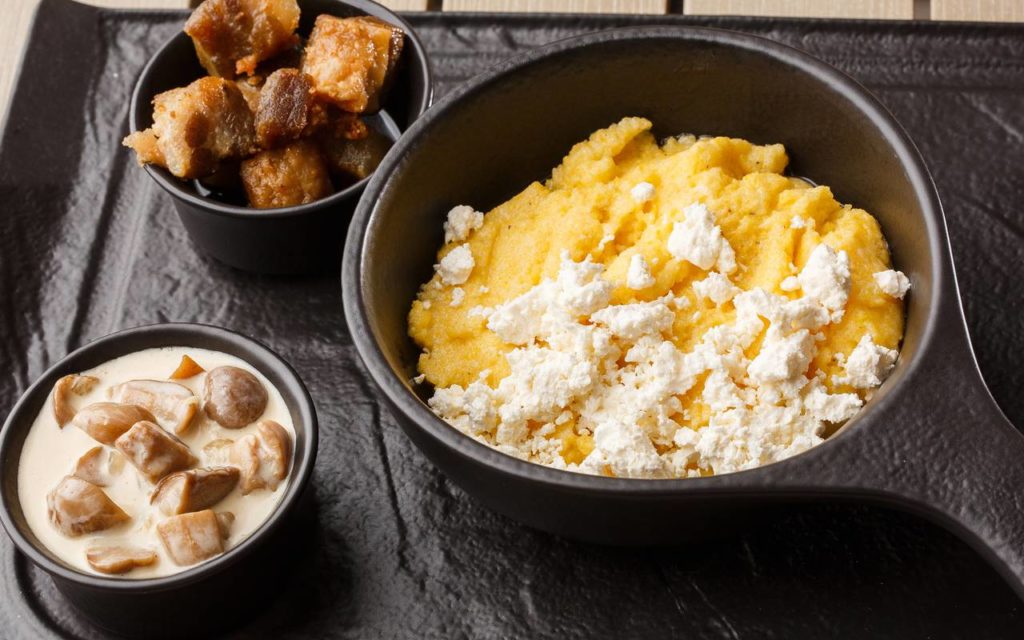 Ukrainian food - polenta or kulesha on a table in a bowl served with cheese and side dishes