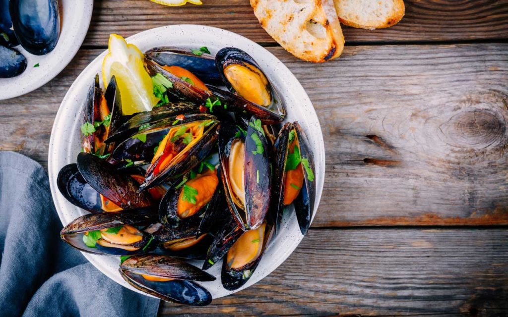 Welsh food: Conwy mussels with a slice of lemon and herbs in a white bowl on a wood table